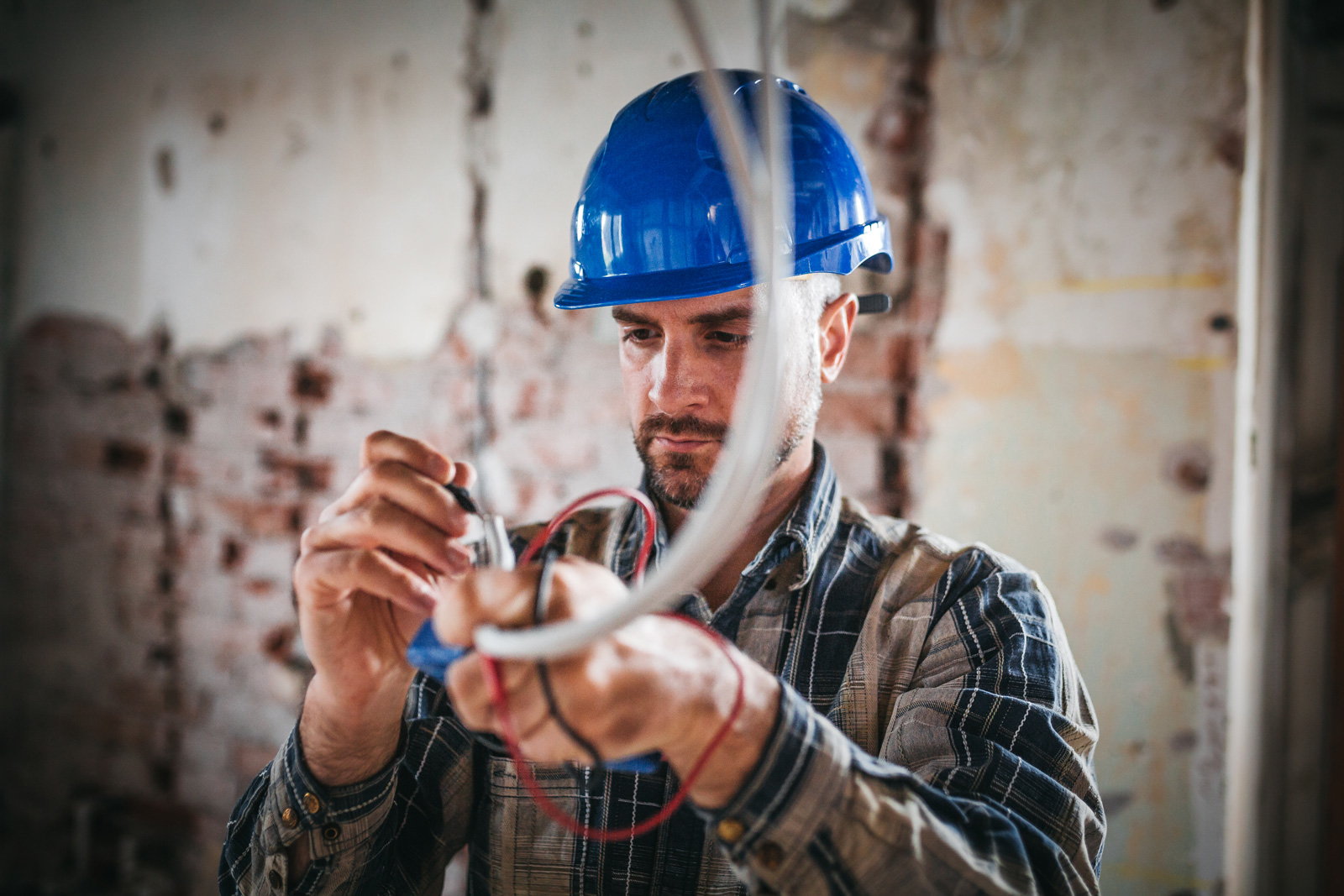 Techniker auf Baustelle mit blauem Helm, der Kabel von der Decke bearbeitet